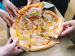 Hands of young people taking pizza slices from delivery cardboard box dining together, friends sharing meal having lunch at home