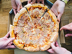 Hands of young people taking pizza slices from delivery cardboard box dining together, friends sharing meal having lunch at home