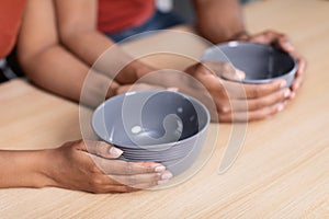 Hands of young starving african american wife and husband holding empty plates at table in kitchen