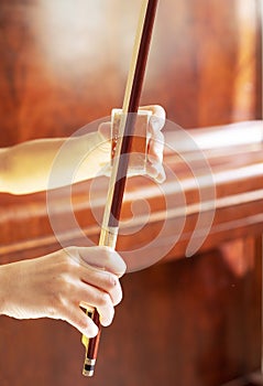 Hands of a young violinist rosin his bow on the background of a piano illuminated by the sun, vertical