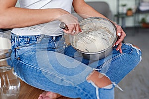 Hands of young woman in casual clothes kneads a dough in a metal plate at stylish kitchen. Young pretty woman baking on