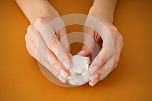 Hands of a young woman with a flower of cotton on a beige background. Female manicure. Close-up