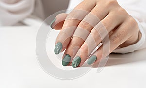 Hands of a young woman with green olive matte nails on a light gray background. Manicure