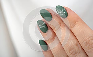 Hands of a young woman with green olive matte nails on a light gray background. Manicure