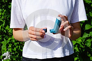 Hands of a young woman holding a blue asthma inhaler outdoors. Pharmaceutical drug for the relief of an asthma attack. Health and