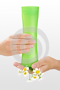 Hands of young woman holding cosmetics bottle and fresh chamomile