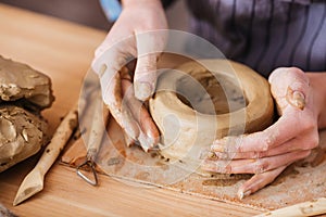 Hands of young woman making earthen pot on wooden table