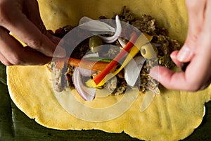 Hands of young woman making venezuelan christmas dish hallacas with all ingredients on table