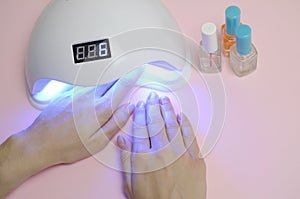 Hands of young woman at manicure procedure close up on pastel pink background