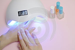 Hands of young woman at manicure procedure close up on pastel pink background