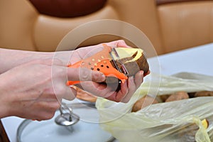 Hands of a young woman peeling potatoes with kitchen utensil on a wooden board