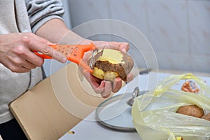 Hands of a young woman peeling potatoes with kitchen utensil on a wooden board photo