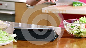 Hands of a young woman preparing a salad using a digital tablet to read a recipe on the Internet