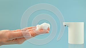 Hands of young woman press the touch button of an automatic soap dispenser on blue background. Concept of hand washing