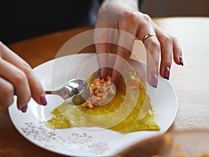 Hands of a young woman putting rice-meat stuffing on a raw sauerkraut leaf with a teaspoon in a plate