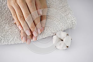 Hands of a young woman, on a white towel, white cotton flower on a white background. Female manicure. Cotton flower