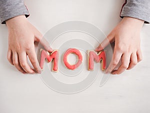 Hands of a younger daughter and word MOM