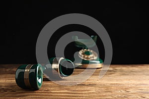 Handset of vintage corded phone on wooden table against black background, closeup