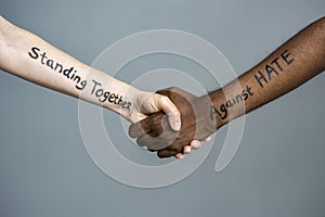 Handshake between black and white human woman and male hands with the message text Standing Together against HATE