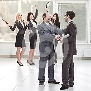 Handshake of business partners on background of cheering business team