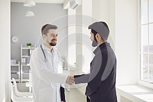 Handshake. Practicing doctor and patient shaking hands smiling at the clinic.