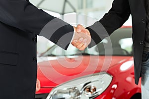 Handshake of two men in suits with a red car