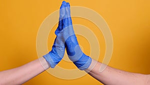 Handshake of two people in blue medical gloves on a yellow background