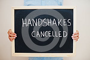 Handshakes cancelled. Coronavirus concept. Boy hold inscription on the board