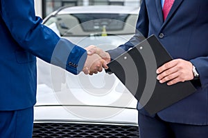 Handshakes of two men against hood of a car