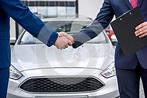 Handshakes of two men against hood of a car