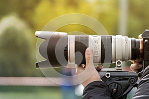 Handshot of a professional photographer outdoors. Man holds a modern camera device. Cameraman shoots outdoors. Shooting with lens.