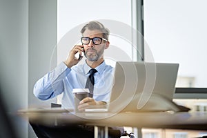 Handsom businessman sitting in the office and using mobile phone and laptop for work