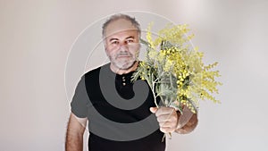 Handsom mature bearded man smiling and giving mimosa flower and heart ballon to viewer. Man with bouquet.Holiday concept. Slow mot