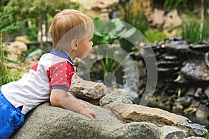 Handsome 3 year old boy child on a walk in the park by the pond on a sunny day