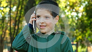 Handsome 6 year old boy talking on the phone while standing in park in autumn.