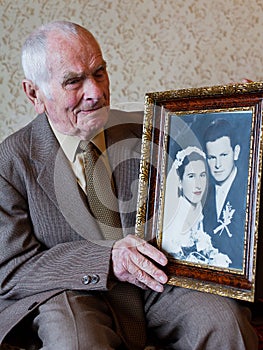 Handsome 80 plus year old senior man holding his wedding photograph. Love forever concept