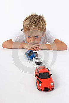 Handsome adorable little boy lying behind a line of car toys with arms crossed and seeming bored photo
