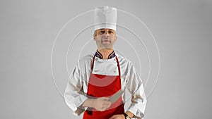 Handsome adult chef turns, he crosses his arms with knive and nods his head on a gray background