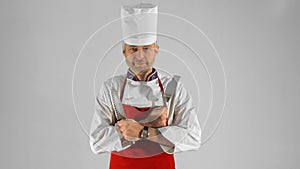 Handsome adult chef turns, he crosses his arms with knive and spatula, he nods his head on a gray background