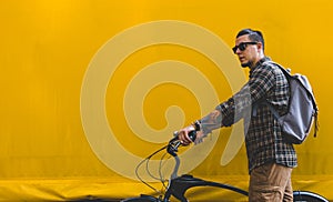 Handsome Adult Man In Sunglasses Walks With A Bicycle Along A Yellow Wall Copy Space