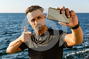handsome adult man taking selfie with smartphone and pointing at camera