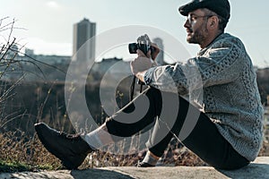 handsome adult man with vintage film camera sitting on rural road on sunny day