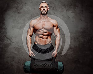 Handsome adult sportsman wearing sportswear posing for a camera while holding a weight bag