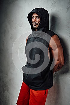 Handsome adult sportsman wearing sportswear posing in a dark studio while leaning on the wall