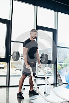 handsome adult sportsman working out with ropes photo