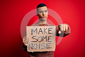 Handsome african american activist man protesting holding banner with make noise message pointing with finger to the camera and to