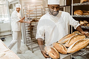 handsome african american baker taking bread loaves from oven