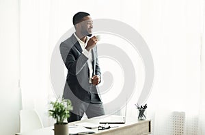 Handsome african american businessman drinking coffee near window in office