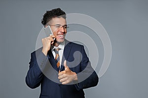 Handsome African-American businessman talking by mobile phone on grey background