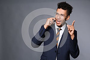 Handsome African-American businessman talking by mobile phone on grey background